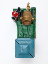 Load image into Gallery viewer, A small sculptural art piece featuring a green textured base with a gold bell, a red-and-black figure, and a blue box-like form at the bottom, photographed against a plain white background.