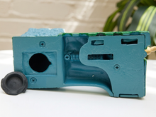 Load image into Gallery viewer, A teal blue plastic replacement part, likely a mechanical or electronic housing component, shown alongside a small black circular cap on a white surface with a blurred background.
