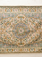Load image into Gallery viewer, An ornate vintage-style tapestry or wall hanging with a detailed floral and medallion pattern in muted pastel colors, displayed against a white painted brick wall.