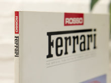 Load image into Gallery viewer, Close-up of a Ferrari book or printed publication showing the title 'Ferrari' in large black letters, a red 'ROSSO' block at the top, and the spine also reading 'ROSSO Ferrari'.