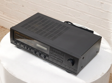 Load image into Gallery viewer, Vintage black Optimus AM/FM stereo receiver with rectangular digital tuner display, large volume knob, front control buttons, and vented top panel