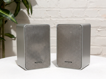 Load image into Gallery viewer, Pair of vintage silver-gray bookshelf stereo speakers with perforated metal front grilles, softly rounded rectangular cabinets, and attached speaker wires