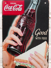 Load image into Gallery viewer, Vintage-style Coca-Cola advertising metal sign with black background, red Coca-Cola logo, illustrated hands holding a glass Coke bottle and sandwich, and Good With Food lettering