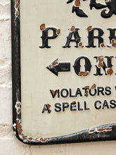 Load image into Gallery viewer, A close-up of a vintage rectangular metal sign with a cream background and black lettering, showing partial text including 'PARK', an arrow, 'VIOLATORS', and 'A SPELL CASE'. The sign has worn, chipped edges with exposed rust-brown metal, mounted against a white painted brick wall.