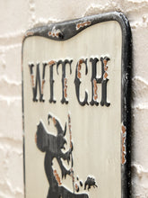 Load image into Gallery viewer, A distressed metal sign with the word 'WITCH' in black gothic letters above a black witch silhouette, mounted against a white brick wall.