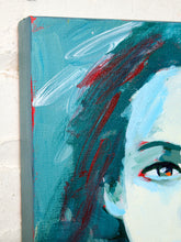 Load image into Gallery viewer, A close-up of a canvas wall art print featuring an abstract portrait of a woman's face with teal, blue, white, and red brushstrokes, shown against a white brick wall.
