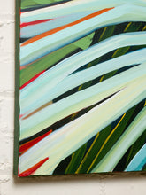 Load image into Gallery viewer, Image 5 of 8: Abstract botanical painting of tropical palm leaves with sweeping diagonal strokes in light blue, green, white, and touches of red and yellow, shown hanging on a white brick wall.