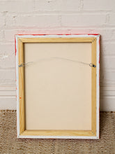 Load image into Gallery viewer, Image 8 of 8: The back side of a rectangular framed canvas or print, showing a light natural wood frame, white painted edges with red paint showing through, and a wire hanging system, set against a white brick wall and woven rug.