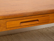 Load image into Gallery viewer, Image 11 of 22: Close-up of a mid-century modern wooden desk featuring a warm honey-toned teak finish, a recessed drawer with a matching curved pull handle, and a textured beige carpet visible underneath.