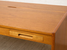 Load image into Gallery viewer, Image 13 of 22: Close-up of a mid-century modern wooden desk with a warm honey-toned finish, featuring a drawer with a recessed pull handle and a cable management slot on the top surface.
