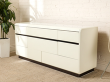 Load image into Gallery viewer, Image 2 of 18: Vintage postmodern white lacquer dresser featuring a long rectangular silhouette, softly rounded corners, asymmetrical geometric drawer fronts, recessed horizontal pulls, and a black plinth base.