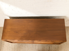 Load image into Gallery viewer, Image 4 of 16: A mid-century modern wooden console table with a warm brown finish, shown from a top-down angle against a white brick wall and textured rug.