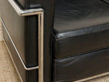Load image into Gallery viewer, Image 12 of 14: Close-up of a black leather armchair with polished chrome tubular metal frame accents, showing the seat cushion, side panel, and leg support on a beige carpet.