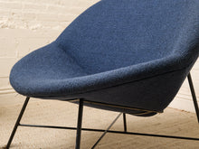 Load image into Gallery viewer, Image 12 of 17: A modern blue upholstered accent chair with a curved seat and back, supported by slim black metal legs, set against a white brick wall and beige carpet.