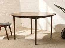 Load image into Gallery viewer, Image 3 of 12: Modern round dining table featuring a warm walnut-tone wood grain finish, subtly segmented circular tabletop border, softly rounded edges, and slender angled tapered legs.