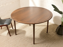 Load image into Gallery viewer, Image 1 of 12: Modern round dining table featuring a warm walnut-tone wood grain finish, subtly segmented circular tabletop border, softly rounded edges, and slender angled tapered legs.