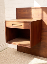 Load image into Gallery viewer, Image 8 of 22: A mid-century modern walnut nightstand with a single drawer and open shelf, mounted against a white brick wall with warm sunlight casting shadows.