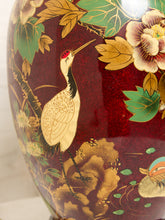 Load image into Gallery viewer, Image 17 of 19: Close-up of a glossy decorative ceramic vase featuring a painted red background with a white crane, gold leaves, flowers, and green foliage.