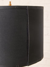 Load image into Gallery viewer, Image 11 of 19: Close-up of a black fabric drum lampshade with visible side seams and a small brass finial at the top, set against a light off-white background.