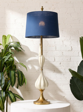 Load image into Gallery viewer, Image 1 of 19: Mid-century table lamp featuring a tall sculptural ivory-toned teardrop body, slender brass-tone stem, rounded brass pedestal base, and deep navy blue cylindrical fabric shade.