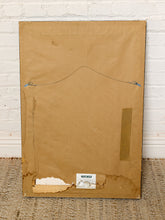 Load image into Gallery viewer, Image 8 of 8: The back of a framed artwork or canvas, showing a large brown cardboard backing, mounting wire, and a small label near the bottom, leaning against a white brick wall on a woven rug.