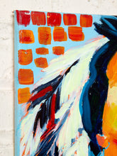 Load image into Gallery viewer, Image 4 of 8: Abstract canvas painting featuring bold brushstrokes of orange, red, white, blue, and yellow on a light blue background, mounted on a white textured wall.
