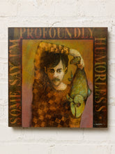 Load image into Gallery viewer, Image 1 of 9: Mixed-media artwork titled Some Say I'm Profoundly Humorless by Robert Bradshaw, depicting a young man in a brown checkered shirt holding a large green fish, with mustard yellow and orange tones and decorative lettering around the composition.
