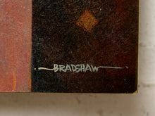 Load image into Gallery viewer, Image 8 of 9: Close-up of a textured dark brown and black square object with a white signature reading BRADSHAW and a small diamond motif near the top, set against a light neutral background.