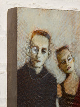Load image into Gallery viewer, Image 4 of 9: A close-up of a textured canvas or print showing a stylized portrait of a man and a woman, photographed against a white brick wall.