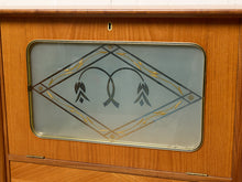 Load image into Gallery viewer, Image 11 of 27: A close-up of a wooden cabinet or door with a rectangular frosted glass panel featuring a decorative black and gold floral diamond design.