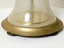 Load image into Gallery viewer, Image 16 of 18: Close-up of the base of a vintage table lamp featuring a clear, textured glass bell and a wide, polished brass-colored metal collar on a white fabric surface.