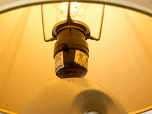 Load image into Gallery viewer, Image 11 of 14: Close-up of a vintage-style light fixture with a brass screw base, clear glass shade, and glowing bulb inside a warm yellow lampshade.