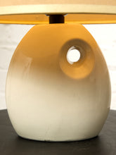 Load image into Gallery viewer, Image 12 of 14: A close-up of a table lamp base with a warm yellow-to-white gradient ceramic body, featuring a circular cutout on the side and a matching yellow lampshade visible at the top.