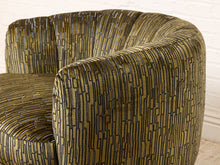 Load image into Gallery viewer, Image 12 of 16: A close-up of a curved armchair upholstered in olive green velvet fabric with a black geometric line pattern, set against a white brick wall background.