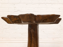 Load image into Gallery viewer, Image 12 of 16: A rustic dark brown wooden pedestal stool or table with a thick cylindrical base and a wide, scalloped top surface, shown against a white painted brick wall.
