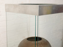 Load image into Gallery viewer, Image 8 of 18: Vintage dark brown sculptural vase with rounded shoulders, a narrow circular opening, tapered body, and weathered surface, displayed inside a tall rectangular glass case with brushed silver-tone metal top and base.