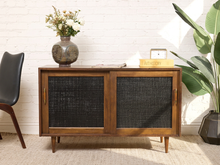 Load image into Gallery viewer, Image 1 of 24: Vintage wooden credenza with two black textured sliding cabinet doors, warm brown wood frame, gold-tone hardware, and short tapered legs