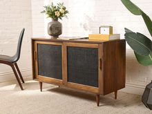 Load image into Gallery viewer, Image 2 of 24: Vintage wooden credenza with two black textured sliding cabinet doors, warm brown wood frame, gold-tone hardware, and short tapered legs
