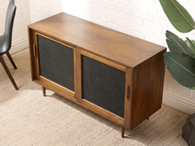 Load image into Gallery viewer, Image 6 of 24: Vintage wooden credenza with two black textured sliding cabinet doors, warm brown wood frame, gold-tone hardware, and short tapered legs