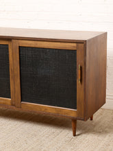 Load image into Gallery viewer, Image 9 of 24: Vintage wooden credenza with two black textured sliding cabinet doors, warm brown wood frame, gold-tone hardware, and short tapered legs
