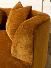 Load image into Gallery viewer, Image 12 of 16: Close-up of a plush velvet sofa in a warm camel brown color, showing the textured fabric and matching throw pillows against a white brick wall background.