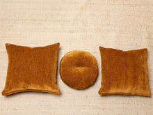 Load image into Gallery viewer, Image 7 of 16: Three textured velvet throw pillows in a warm rust-orange color, arranged on a neutral beige woven rug. The set includes two square pillows and one round tufted pillow.