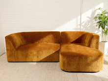 Load image into Gallery viewer, Image 6 of 16: Bonnie Two-Piece Sectional Sofa in Thriller Amber featuring golden amber textured upholstery, rounded arms, generously cushioned seating, a right-facing curved chaise, two square accent pillows, and a matching round tufted pillow.