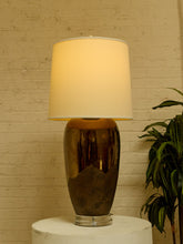 Load image into Gallery viewer, Image 2 of 17: Vintage table lamp featuring a tall rounded body with a reflective dark metallic upper finish, textured charcoal lower section, clear Lucite-style circular base, and illuminated ivory cylindrical drum shade.