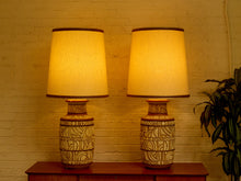 Load image into Gallery viewer, Image 8 of 21: Pair of matching vintage table lamps featuring rounded ivory-colored bases with intricate brown geometric patterns, circular and linear motifs, and tall tapered cream fabric shades with decorative trim.