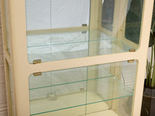 Load image into Gallery viewer, Image 11 of 24: Cream-colored wooden display cabinet with glass doors and three glass shelves, photographed indoors against a white tent-like backdrop.