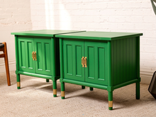 Load image into Gallery viewer, Image 2 of 21: Pair of vintage Kelly green cabinet nightstands featuring vibrant green painted finishes, vertical fluted side panels, two paneled cabinet doors each, brass-tone handles, square inset tops, and slender legs with brass-tone feet.