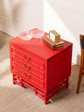 Load image into Gallery viewer, Image 6 of 21: A bright red side table with four drawers and decorative brass handles, styled with two clear glass bowls and a small stack of books on top, set against a white brick wall and beige carpet.