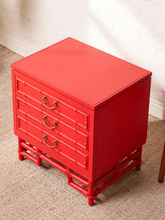 Load image into Gallery viewer, Image 9 of 21: A bright red nightstand with a bamboo-inspired frame design, three drawers with brass handles, and a flat top, shown on a carpeted floor against a white brick wall.