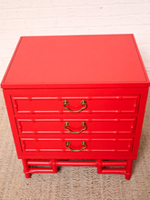Load image into Gallery viewer, Image 10 of 21: A bright red three-drawer nightstand with a bamboo-inspired design, featuring brass metal drawer pulls, set against a white brick wall and textured beige carpet.